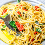 A fork lifts spaghetti with cherry tomatoes and spinach from a plate, glistening with olive oil and herbs—an inviting one pot Tuscan spaghetti that captures the essence of a rustic Italian dinner.