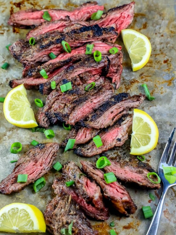 Grilled flank steak with lemon slices cooked on a baking sheet.
