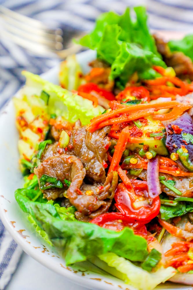 lettuce on a plate with beef, carrots, tomatoes, and kimchi dressing.