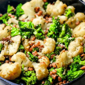 Sautéed cauliflower and broccoli florets mixed with small pieces of browned meat in a skillet, inspired by skillet roasted broccoli and cauliflower recipes.