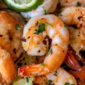 Close-up of Cilantro Lime Saut&eacute;ed Shrimp garnished with chopped herbs, red pepper flakes, and lime wedges&mdash;perfect for those wanting to learn how to cook shrimp with a fresh, zesty twist.