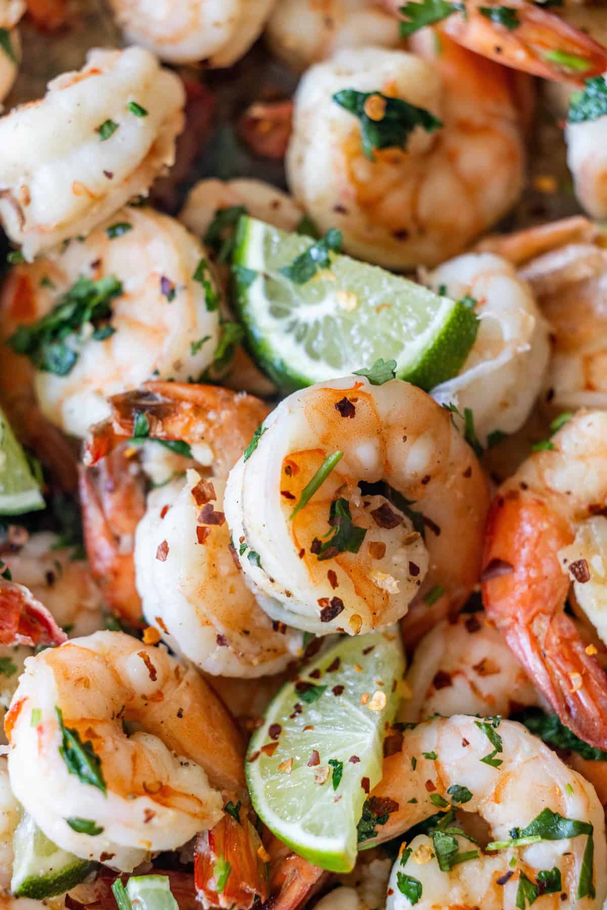 Close-up of Easy Cilantro Lime Shrimp, cooked to perfection and garnished with chopped herbs, red pepper flakes, and lime wedges&mdash;a delicious answer for how to cook shrimp that doesn't taste fishy.