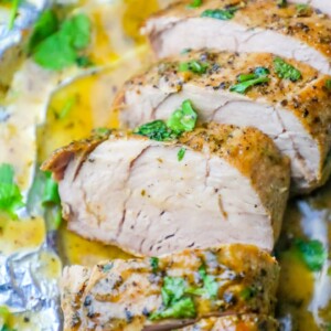Picture of pork tenderloin sliced and garnished with parsley on tinfoil.