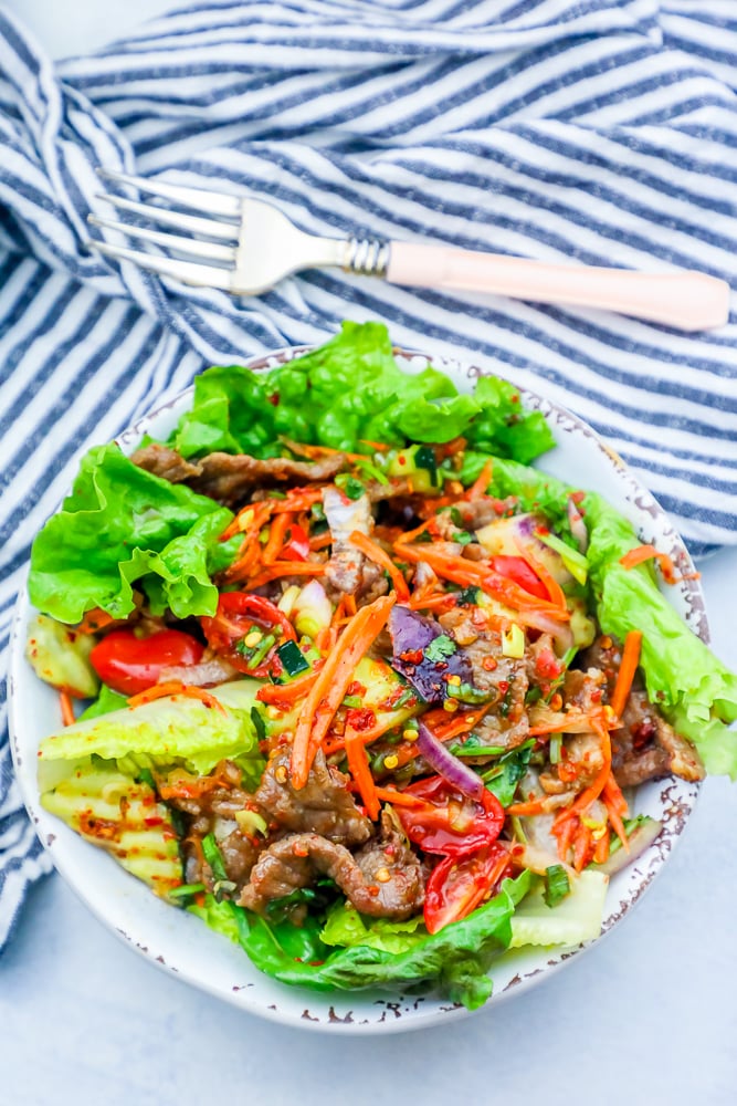 lettuce on a plate with beef, carrots, tomatoes, and kimchi dressing.