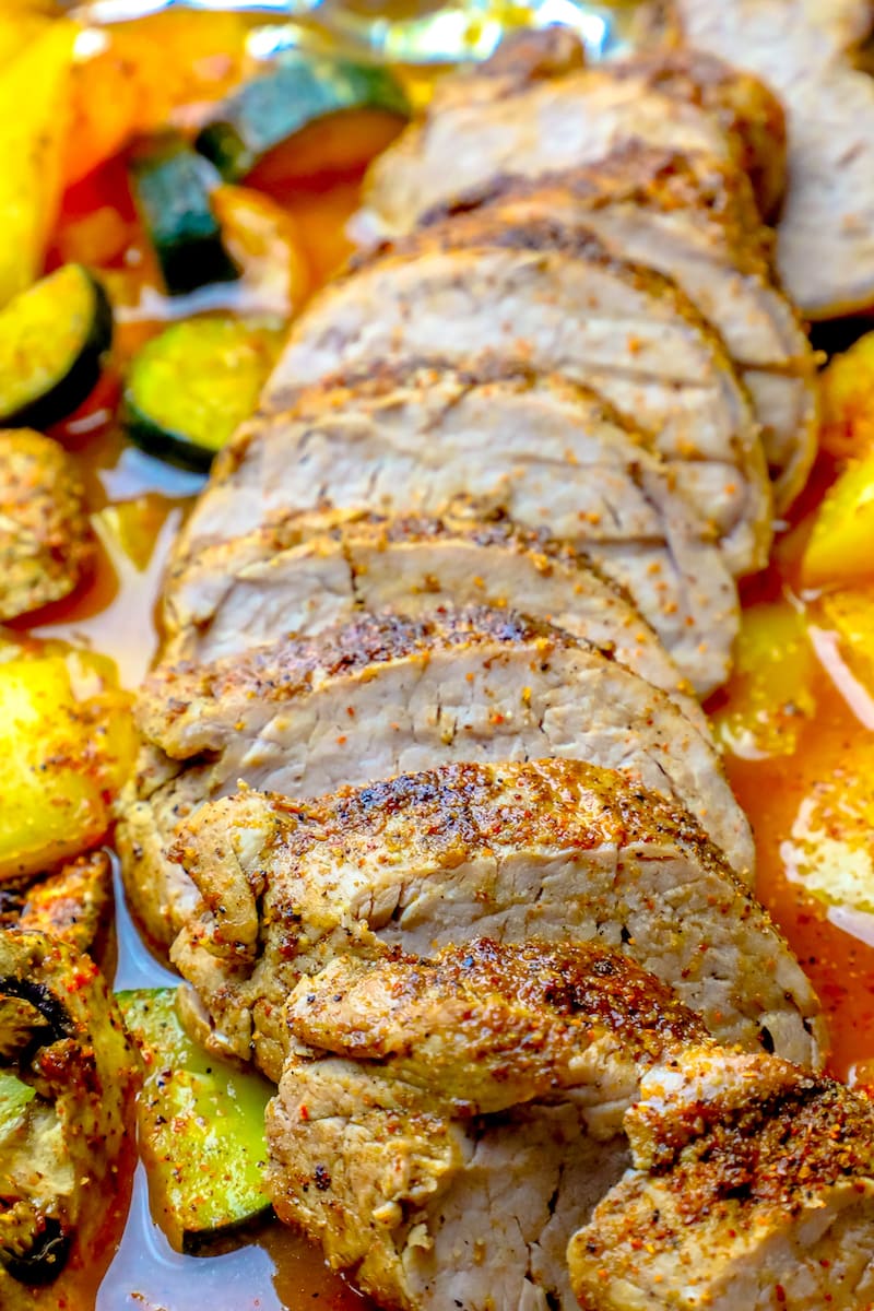 picture of sliced pork tenderloin with cajun seasoning on a baking tray with vegetables. 
