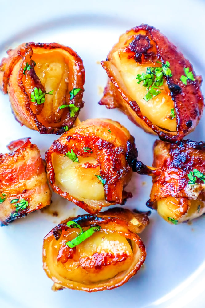 picture of bacon wrapped scallops with a brown sugar glaze on a white plate with chopped parsley on top 