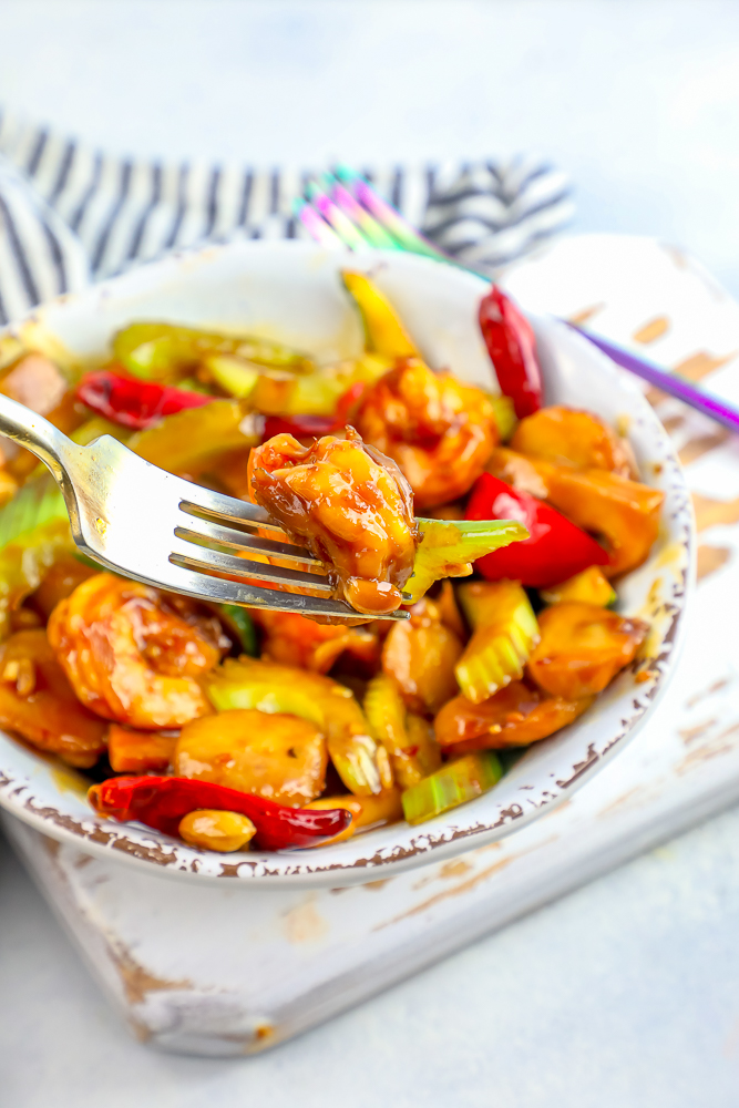 kung pao shrimp and vegetables on a fork over a bowl of kung pao shrimp picture