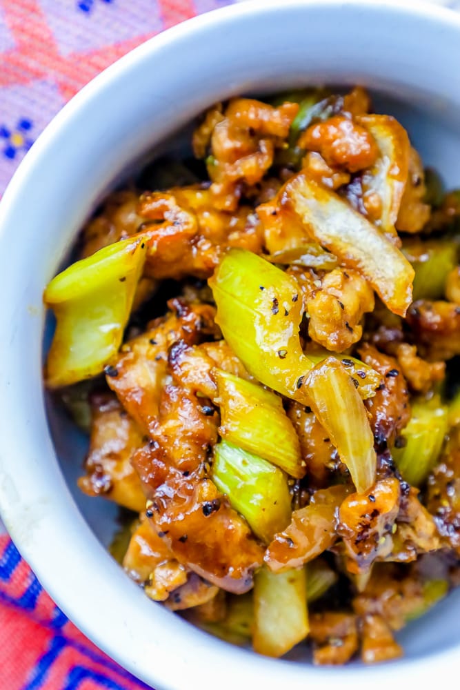 chicken and vegetables in black pepper sauce in a white bowl