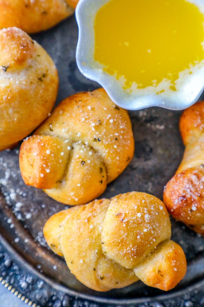 baked garlic knots dusted with parmesan and herbs next to a cup of melted butter on a platter