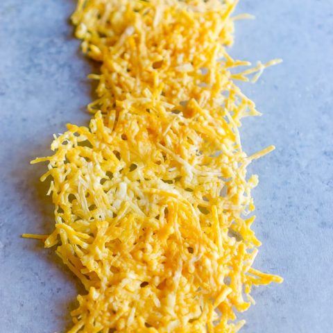 Easy Baked Parmesan Crisps Recipe with shredded cheese on a blue surface.