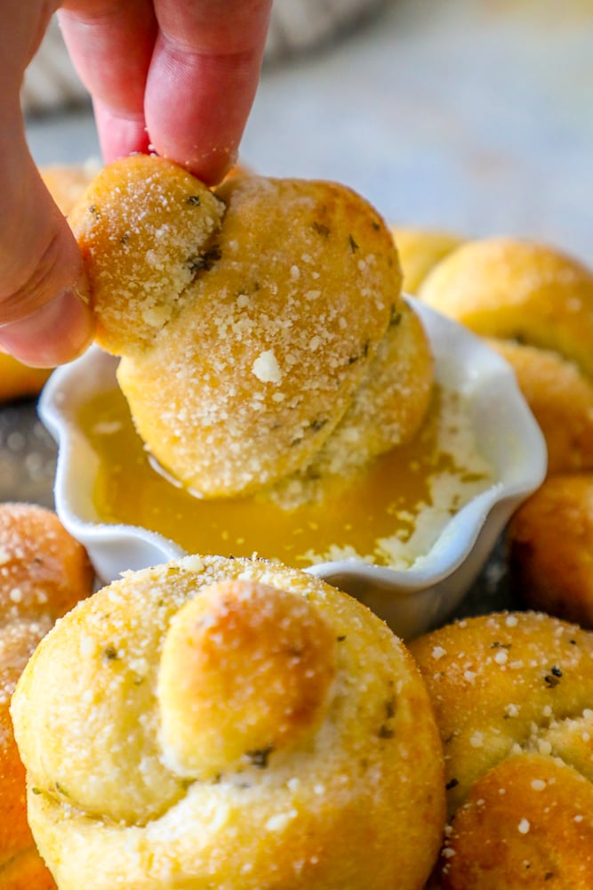 baked garlic knots dusted with parmesan and herbs next to a cup of melted butter on a platter