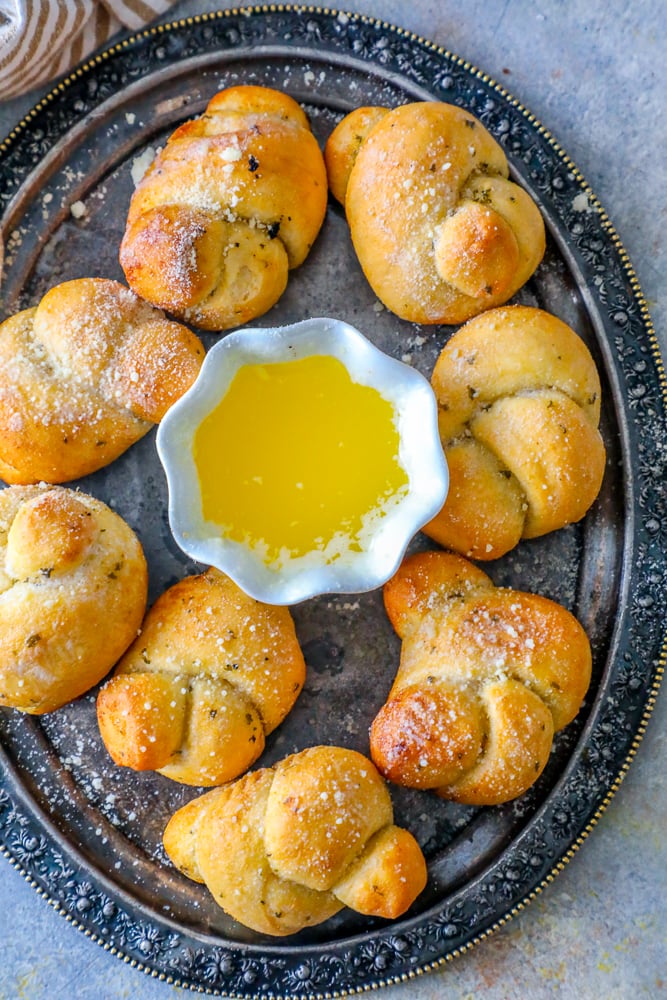 baked garlic knots dusted with parmesan and herbs next to a cup of melted butter on a platter