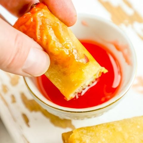 A person is dipping a homemade spring roll in a sauce.