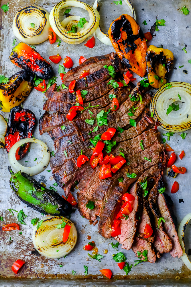 sliced steak on a platter with chiles and charred vegetables in the background