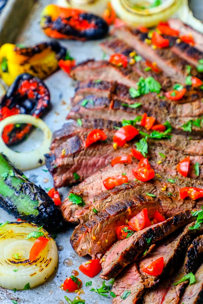 sliced steak on a platter with chiles and charred vegetables in the background