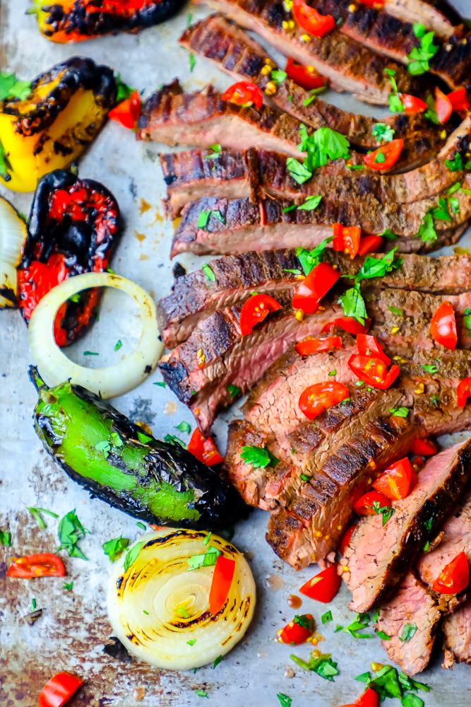 sliced steak on a platter with chiles and charred vegetables in the background