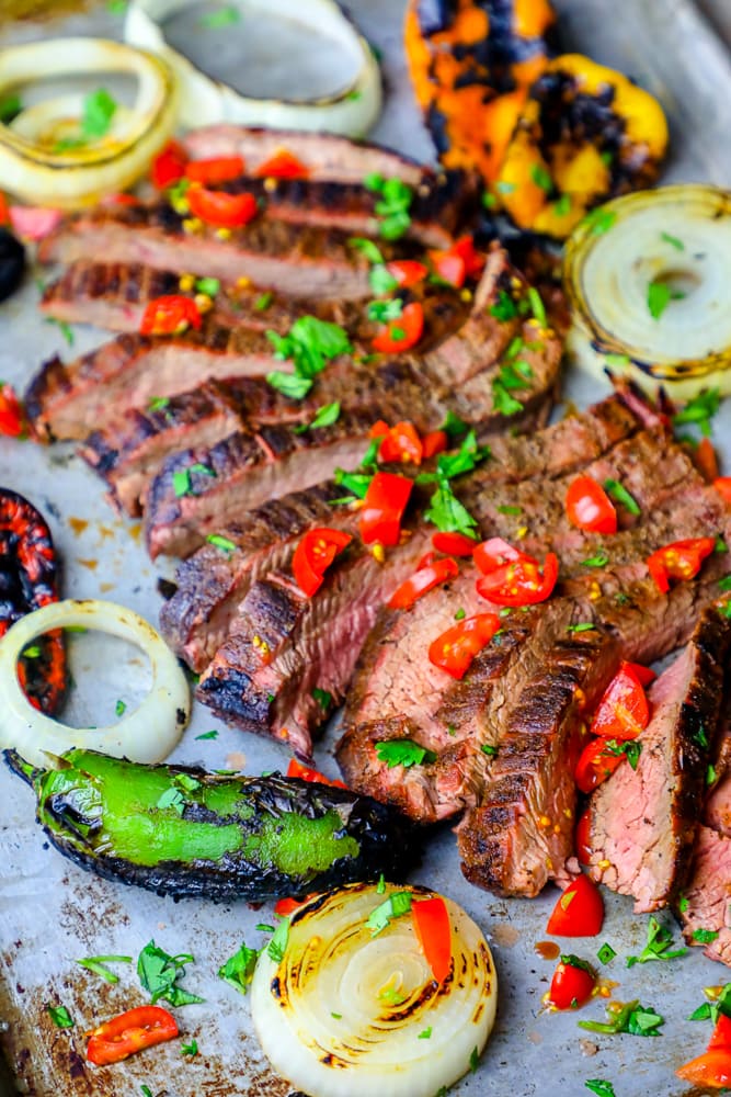 sliced steak on a platter with chiles and charred vegetables in the background