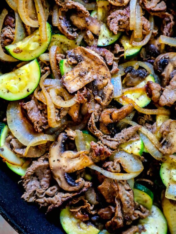 A skillet filled with zucchini and onions cooked alongside thin sliced top sirloin for a delicious dinner.