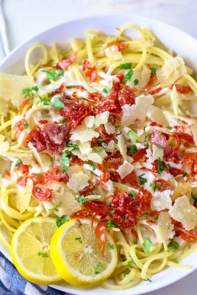 Creamy lemon pasta with bacon and lemon wedges.