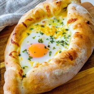 picture of baked khachapuri on a cutting board with egg on top