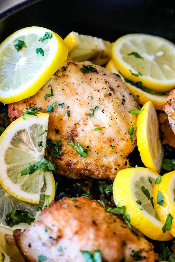 chopped cilantro and sliced lemons in a pan with baked chicken thighs