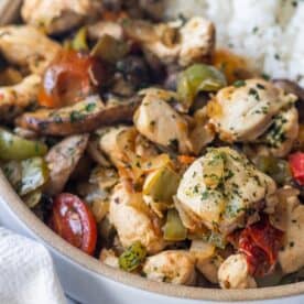 A close-up of a bowl filled with cooked chicken pieces, bell peppers, tomatoes, and herbs—this Keto Italian Chicken Skillet Dinner is served with a portion of white rice visible in the background.