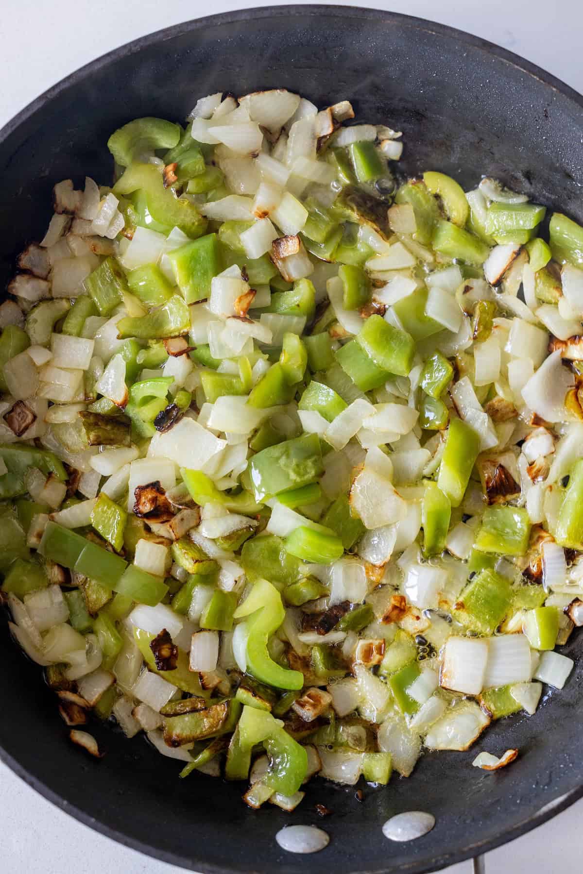 Chopped green bell peppers and onions cooking in a black skillet, just like the perfect start for a 20 minute Italian chicken and vegetables skillet, with some pieces lightly browned.