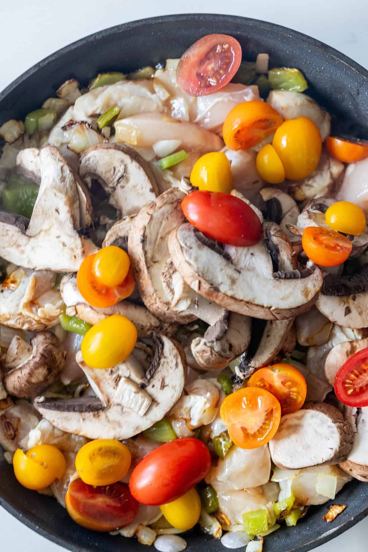 A skillet filled with sliced mushrooms, cherry tomatoes, diced onions, and chopped green peppers—perfect for starting a delicious Italian Chicken and Vegetables dish.