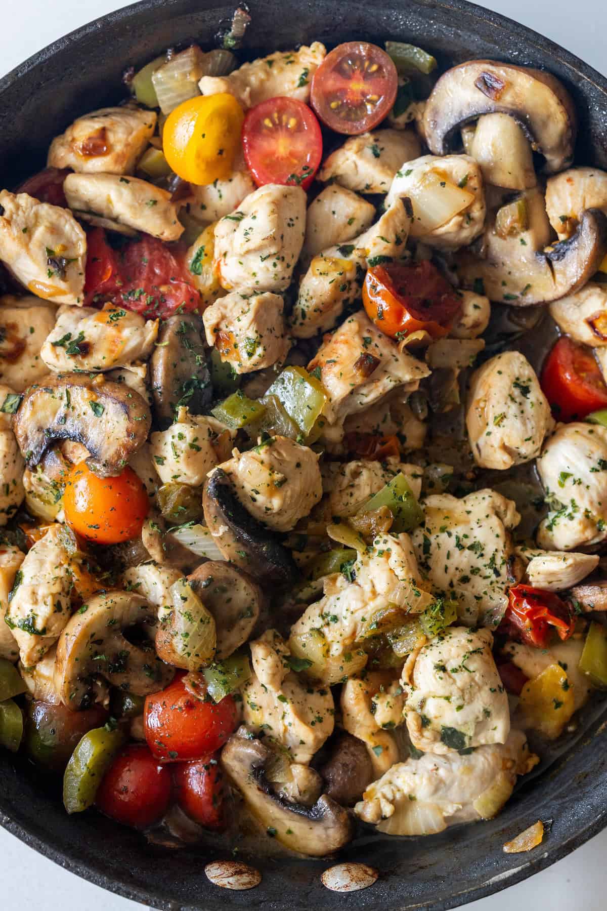 A Keto Italian Chicken Skillet Dinner featuring cooked chicken, mushrooms, cherry tomatoes, onions, and green bell peppers, all garnished with fresh herbs.