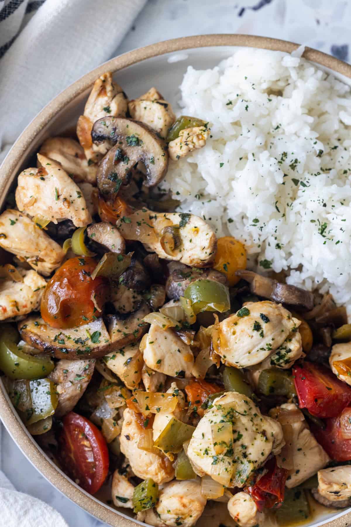 A bowl of white rice served with sautéed chicken, mushrooms, bell peppers, tomatoes, and herbs—just like a 20 minute Italian chicken and vegetables skillet.