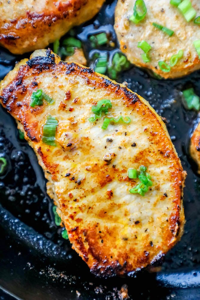 a baked pork chop in a cast iron pan with chives on top