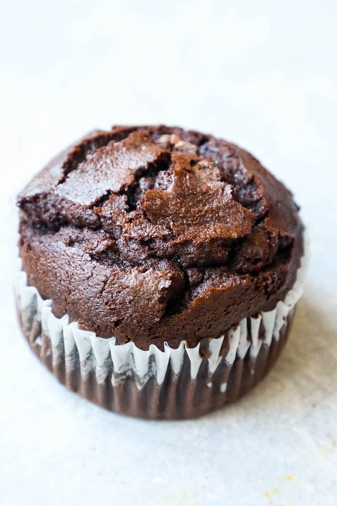 A close up of moist chocolate chunk muffins on a white surface.