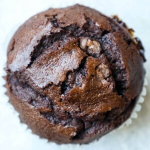 A close up of a moist chocolate chunk muffin on a white surface.