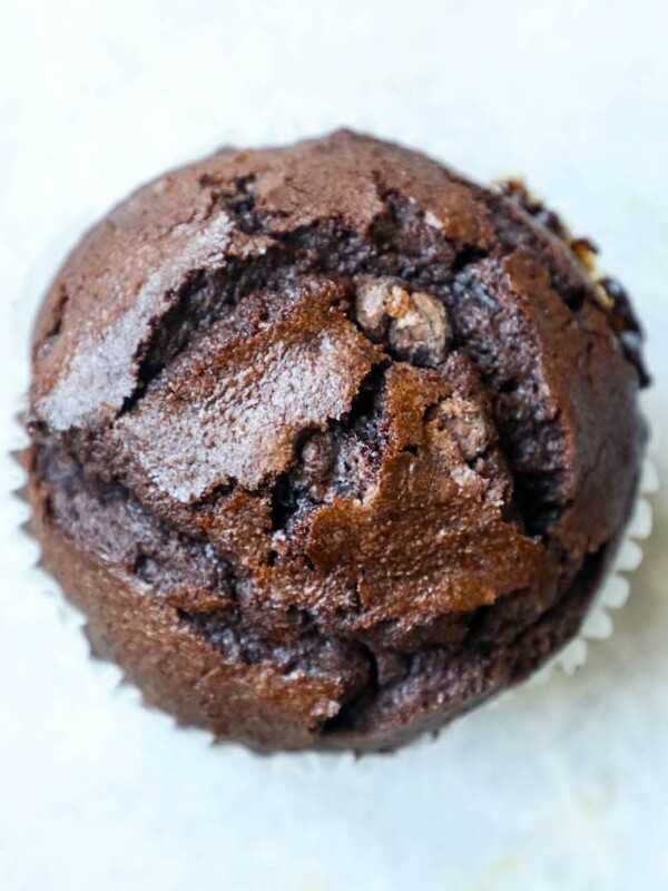 A close up of a moist chocolate chunk muffin on a white surface.
