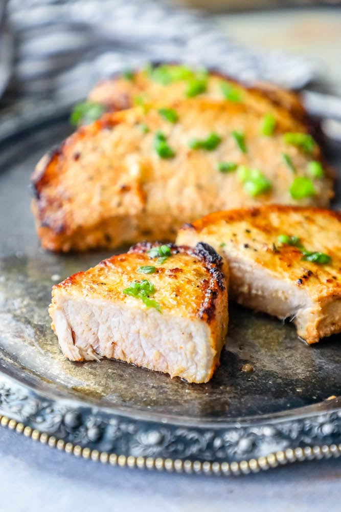 Picture of a baked pork chop on a plate with chives on top