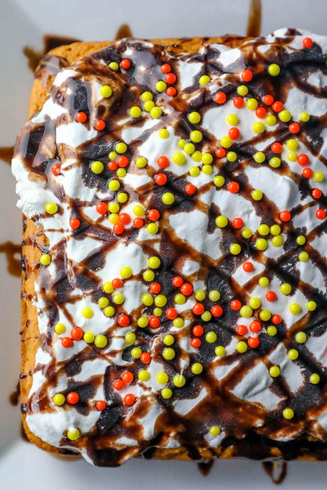 pumpkin cake with white frosting chocolate drizzle and orange and yellow sprinkles on top. 