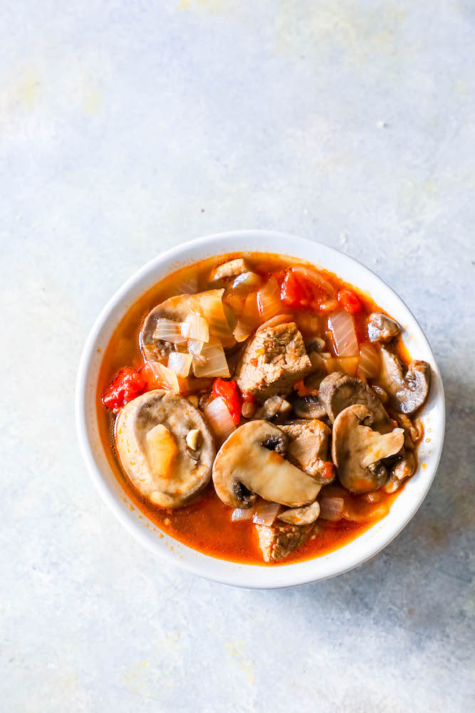 bowl of soup with steak, mushrooms, tomatoes, onions, and stock