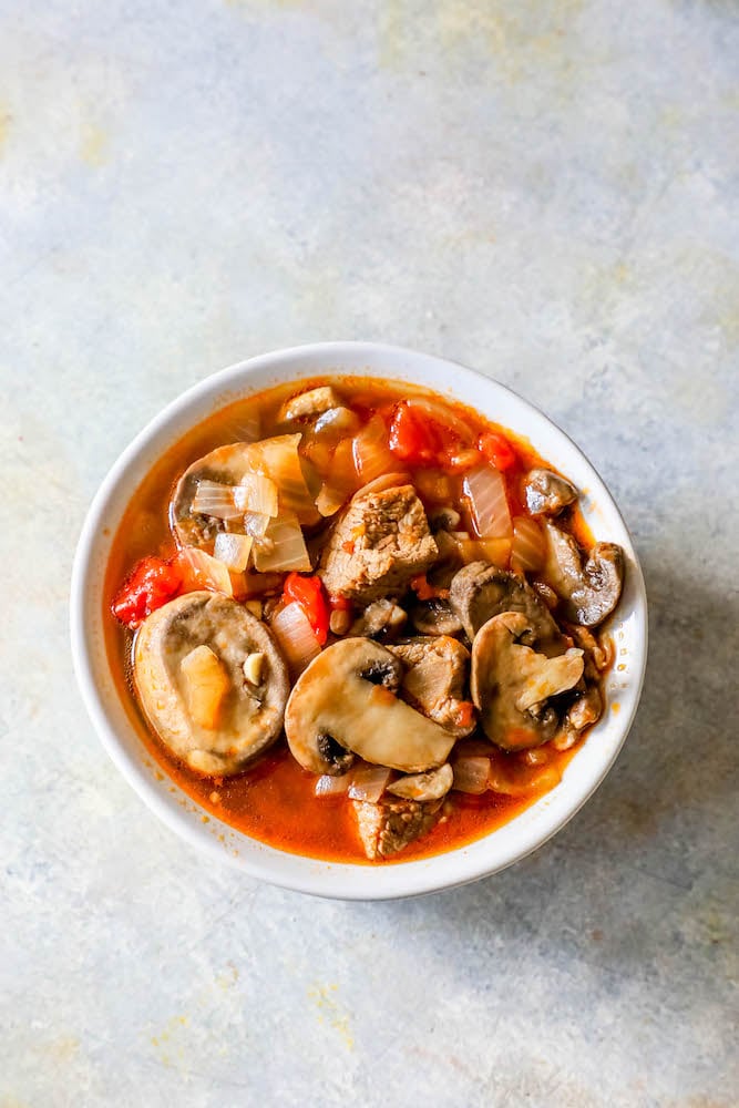 bowl of soup with steak, mushrooms, tomatoes, onions, and stock