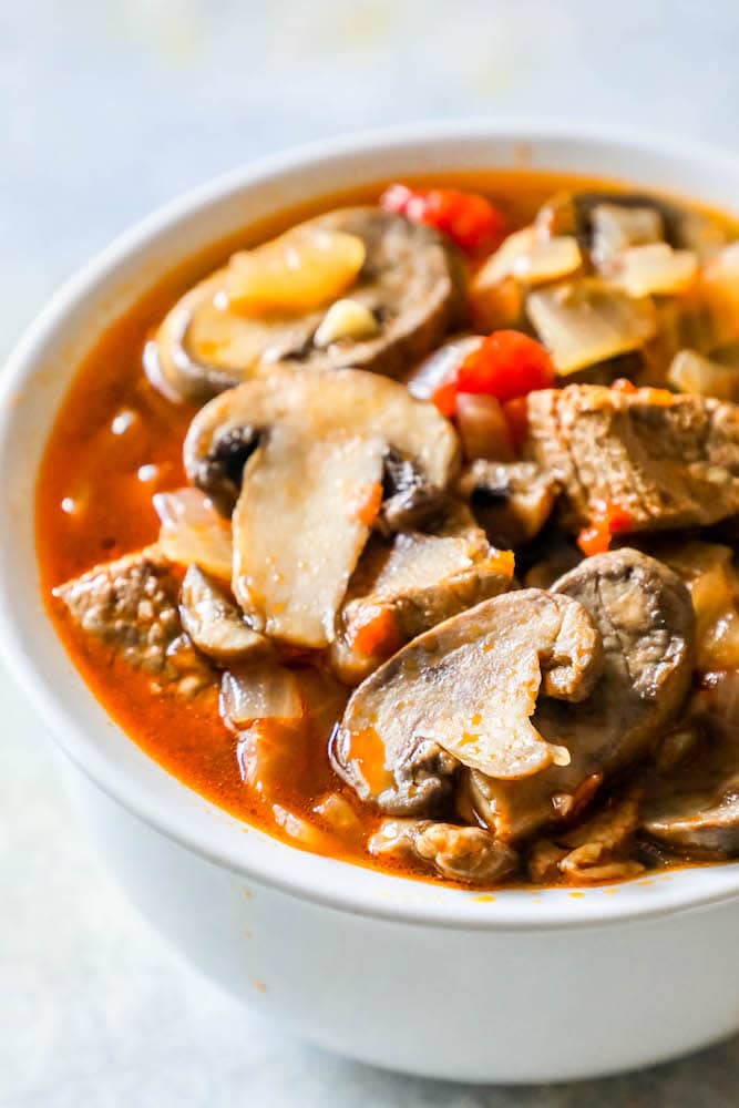 bowl of soup with steak, mushrooms, tomatoes, onions, and stock