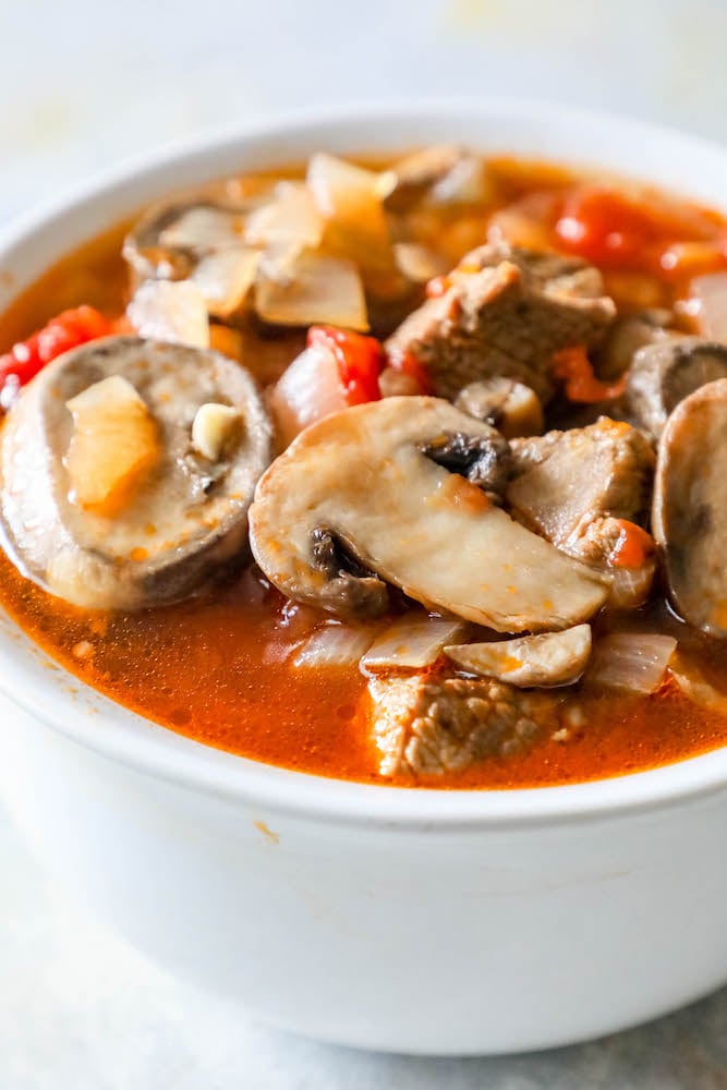 bowl of soup with steak, mushrooms, tomatoes, onions, and stock