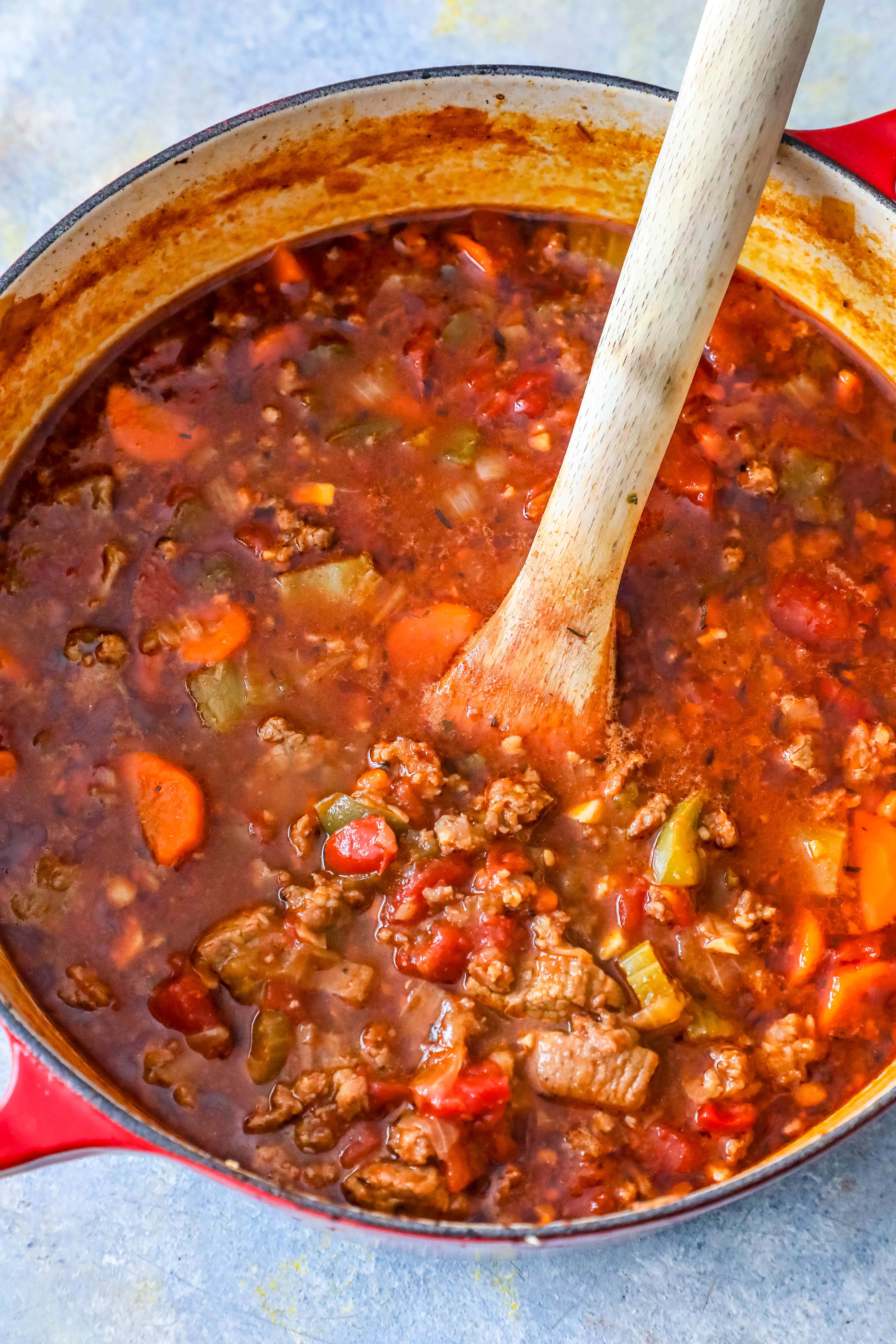 steak and beef chili in a large red pot with a wooden spoon 