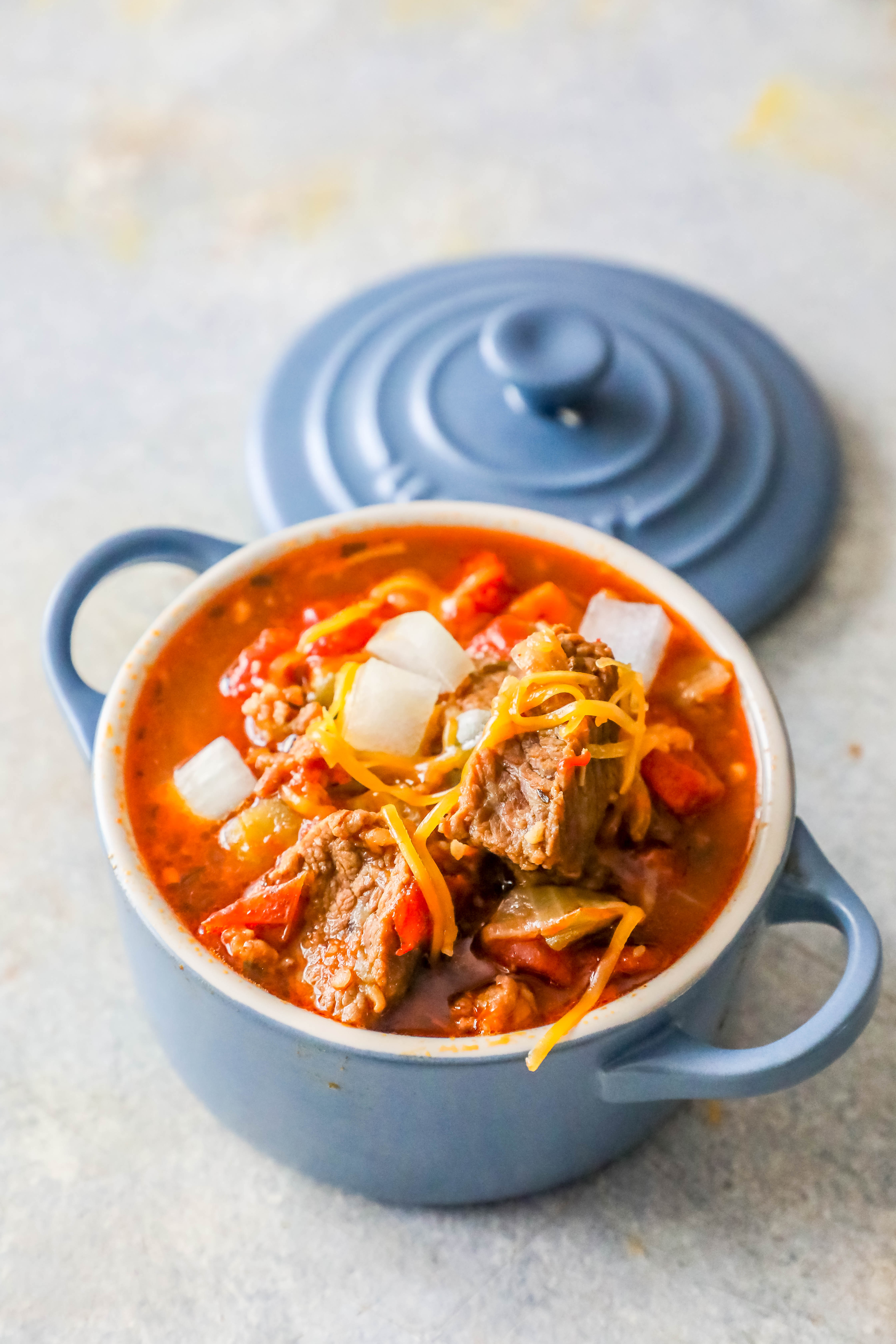 steak chili in a blue bowl with handles and shredded cheese on top 