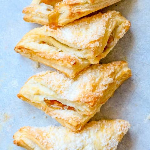 A stack of easy apple turnovers with powdered sugar on a blue background.