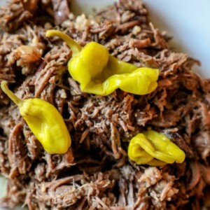 A plate of delicious pulled pork with peppers on it, prepared using the Best Slow Cooker Mississippi Roast Recipe.