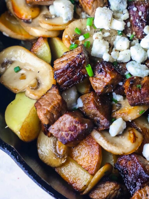 A skillet filled with steak, potatoes, and feta cheese.