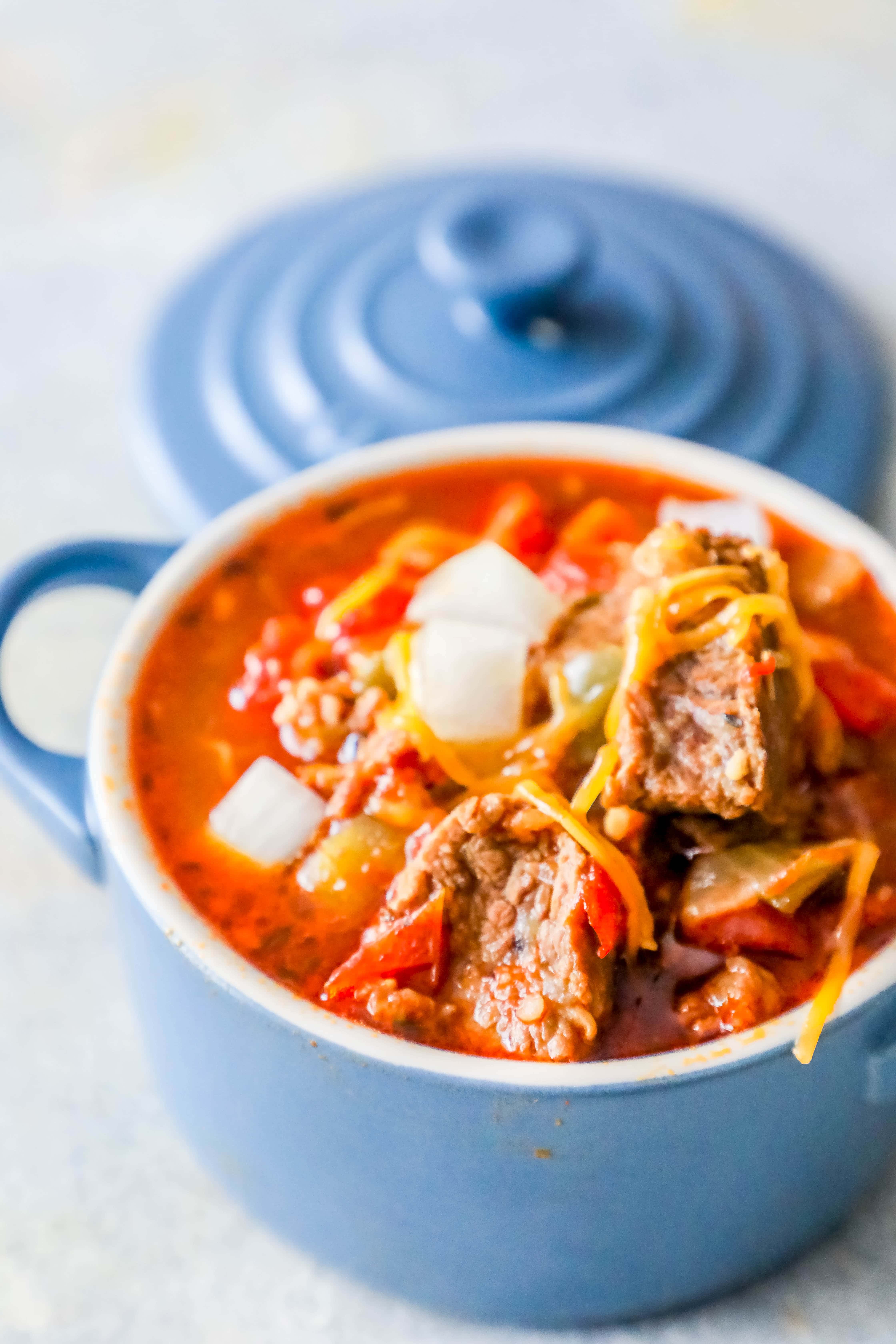 steak chunk chili with vegetables and shredded cheese on top in a blue bowl 