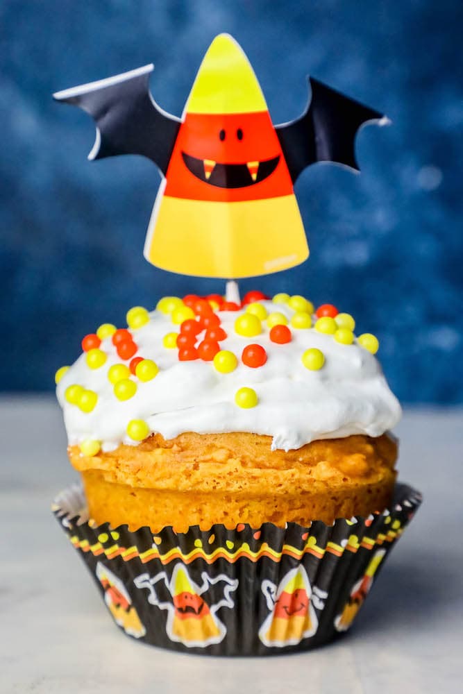 picture of a pumpkin cupcakes with white frosting and orange and yellow sprinkles and candycorn bats