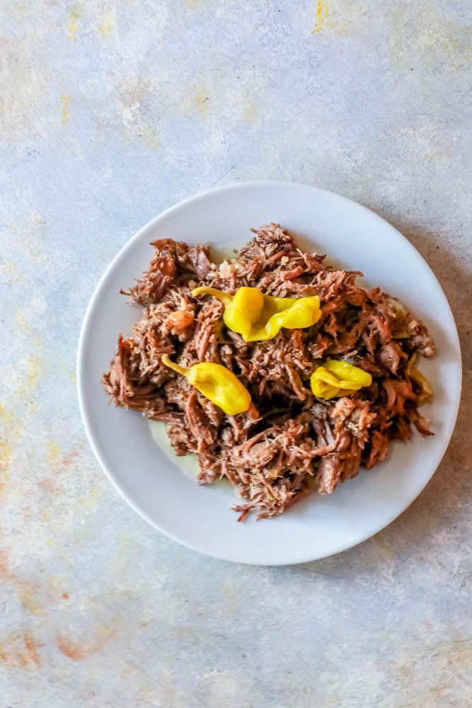 picture of a plate sitting on a countertop with pulled roast and Pepperoncini pepperss