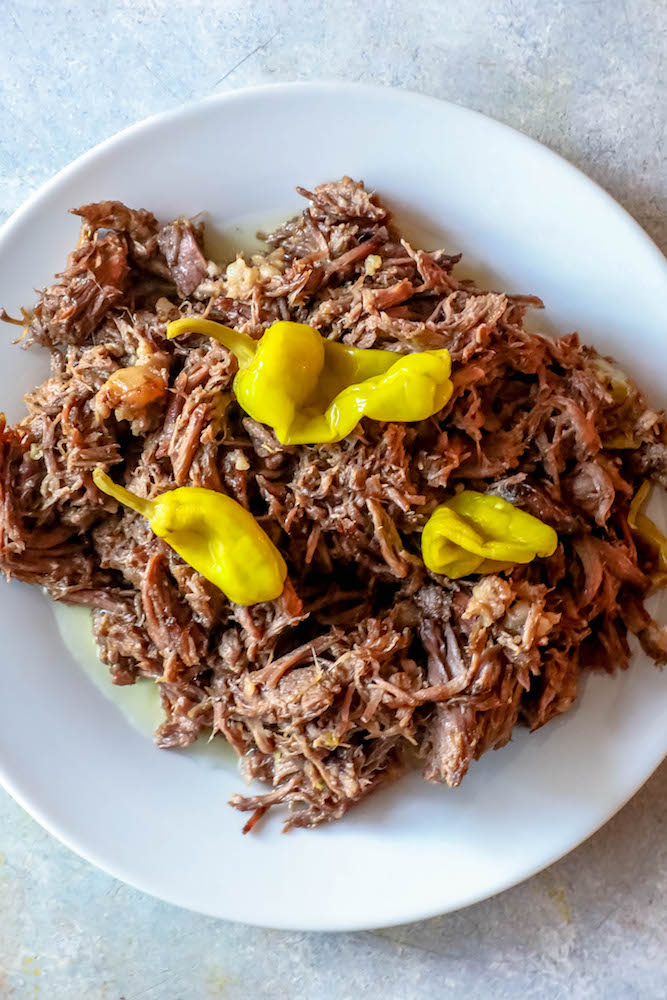 picture of shredded roast with pepperoncini peppers on a white plate