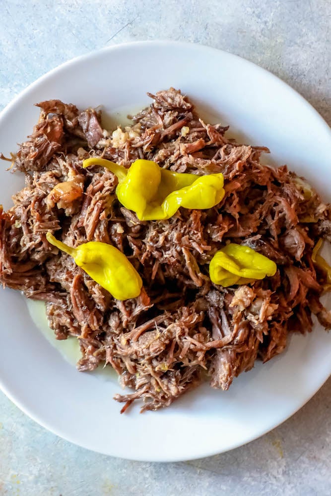 picture of shredded roast with pepperoncini peppers on a white plate